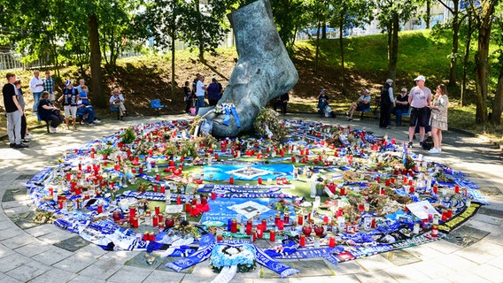 Blumen und Kerzen stehen vor der Trauerfeier um Uwe Seelers Bronzefuß herum. © picture alliance/dpa | Daniel Bockwoldt 