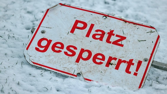 Ein Schild mit der Aufschrift "Spielabsage" liegt auf einem schneebedecktem Rasen. © IMAGO / HMB-Media 