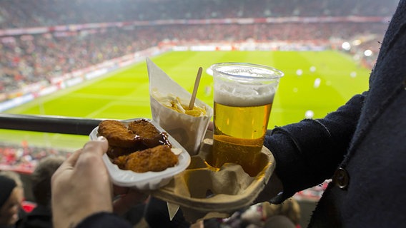 Ein Fußball-Fan hat Hähnchen, Pommes und Bier in der Hand. © imago / ActionPictures 