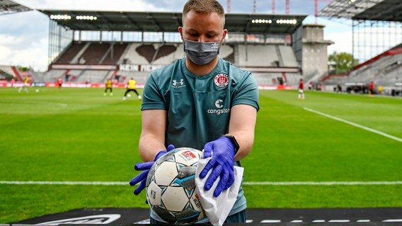 Ein Mitarbeiter des FC St. Pauli wischt einen Spielball ab. © picture alliance/dpa Foto: Axel Heimken