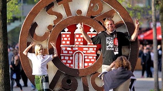 Eine Familie fotografiert sich am Hamburger Millerntorstadion vor dem Vereinslogo vom FC St. Pauli. © dpa 