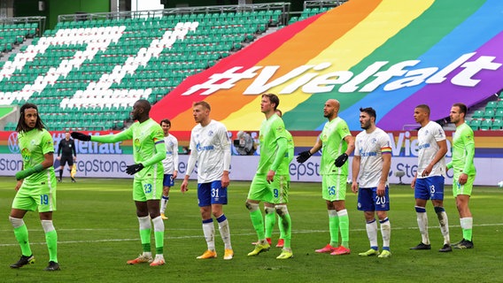 An image from the 2020/2021 Bundesliga season shows players from VfL Wolfsburg and Schalke 04 in front of a rainbow engraved banner. 