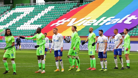 Ein Foto aus der Bundesliga-Saison 2020/2021 zeigt Spieler des VfL Wolfsburg und von Schalke 04 vor einem Transparent in Regenbogenfarben mit der Aufschrift "#Vielfalt". © picture alliance / augenklick/Ralf Ibing /firo Spor | firo Sportphoto/Ralf Ibing 