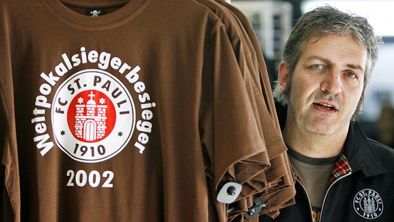 Hendrik Lüttmer präsentiert das von iohm erfundene "Weltpokalsiegerbesieger-T-Shirt" des FC St. Pauli. © picture-alliance/ dpa Foto: Maurizio Gambarini