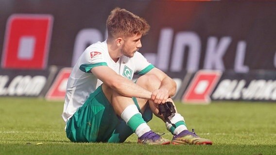 Werder Bremens Profi Romano Schmid sitzt frustriert auf dem Rasen. © IMAGO / Nordphoto 