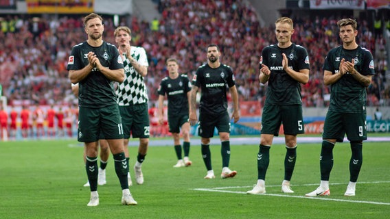 Die Werder-Profis Niclas Füllkrug (l.), Amos Pieper (2.v.r.) und Dawid Kowniaki (r.) bedanken sich bei den mitgereisten Fans. © IMAGO / Eibner 