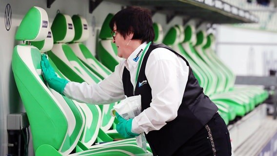 Eine Reinigungskraft desinfiziert die Auswechselbänke im Stadion des VfL Wolfsburg. © imago images/Picture Point LE 