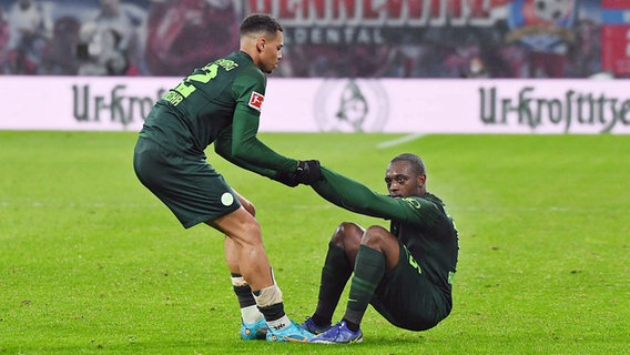 Wolfsburgs Felix Nmecha (l.) hilft Jerome Roussillon auf die Beine. © IMAGO / opokupix 