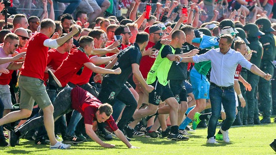 Hannovers Manager Horst Heldt (r.) sowie Fans und Ersatzspieler rennen auf den Rasen. © imago/foto2press 