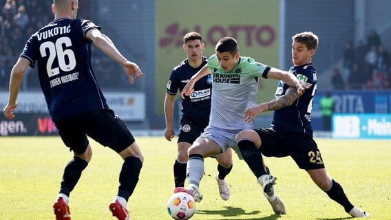 Hannovers Nicola Tresoldi (M.) kämpft gegen Wiesbadens Aleksandar Vukotic, Robin Heußer und Marcus Mathisen (v.l.) um den Ball. © IMAGO / Jan Huebner 