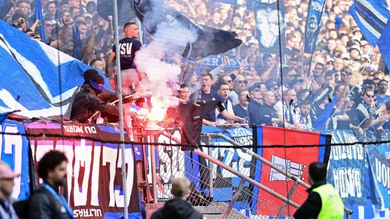 HSV-Fans zeigen ein Textil mit dem Schriftzug Polizei und brennen einen Bengalo ab. © Witters Foto: Tay Duc Lam