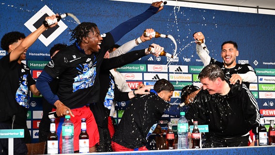 HSV-Trainer Merlin Polzin (r.) wird auf der Pressekonferenz nach dem Aufstieg von seinen Spielern mit einer "Bierdusche" überrascht. © Witters/LeonieHorky 