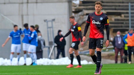 Kiels Benedikt Pichler ist enttäuscht, während Darmstadts Spieler im Hintergrund einen Treffer bejubeln. © IMAGO / Eibner 
