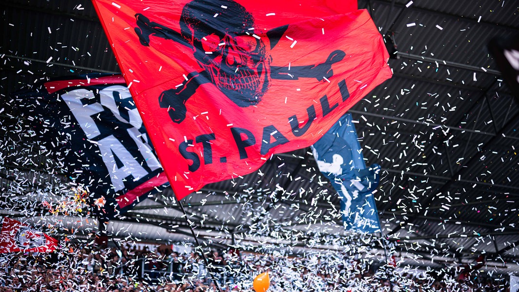 Fans des FC St. Pauli schwenken Fahnen und werfen Konfetti.