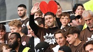 St.-Pauli-Trainer Fabian Hürzeler feiert den Bundesliga-Aufstieg inmitten der Fans und vor einem Herz-Transparent. © IMAGO / Nordphoto 