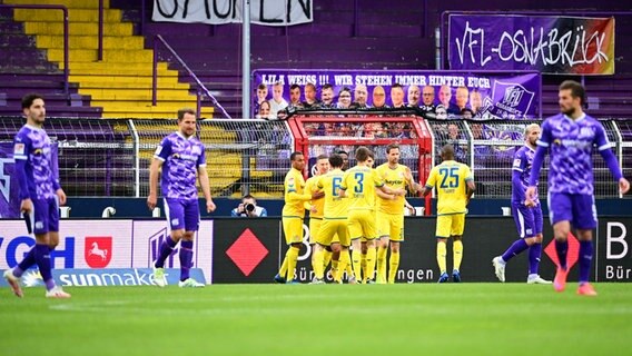 Braunschweigs Spieler bejubeln im Hintergrund einen Treffer, während Osnabrücks Spieler bedient sind. © IMAGO / Revierfoto 