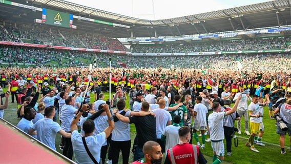 Bremens Spieler bejubeln den Aufstieg in die Bundesliga und feiern vor den Fans, die den Platz zuvor gestürmt haben. © IMAGO / Kirchner-Media 