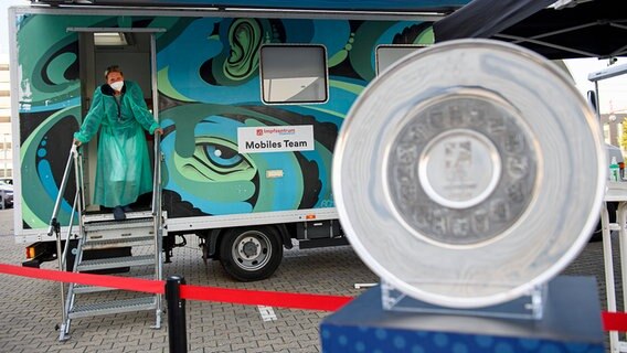 Ein mobiles Impfzentrum beim Handball-Supercup 2021, davor die deutsche Meisterschale © imago images/Sven Simon 