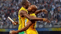 Usain Bolt und sein Teamkollege Asafa Powell feiern ihre Goldmedaille im 4x100-m-Lauf. © AP Foto: Mark J. Terrill