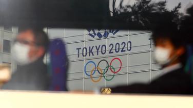 Zugpassagiere mit Atemschutz vor dem Olympia-Banner in Tokio © imago images/AFLO 