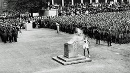 Ein Läufer entzündet das olympische Feuer im Berliner Lustgarten. © picture-alliance / IMAGNO/Austrian Archives 