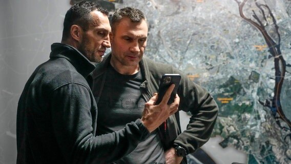 Wladimir (l.) und Vitali Klitschko schauen auf ein Handy. © picture alliance/dpa/AP | Efrem Lukatsky 