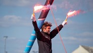 Boris Herrmann hält bei der Einfahrt nach Les Sables-d'Olonne zwei Bengalos hoch. © Marie Lefloch / Team Malizia 