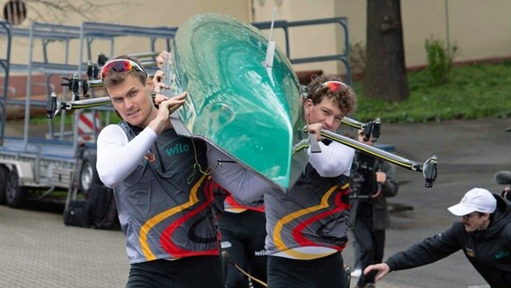 Hannes Ocik (l.) und Mark Hinrichs tragen das Achter-Ruderboot. © IMAGO / Sven Simon 