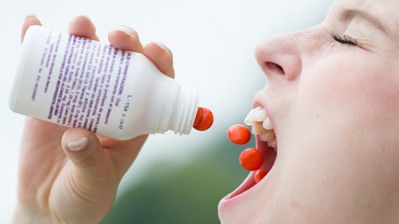 Eine Frau schüttet sich rote Pillen in den Mund © picture alliance / dpa | Friso Gentsch 