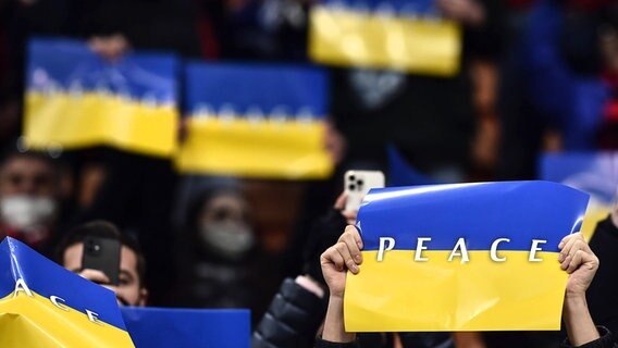 Zuschauer eines Fußballspiels halten Plakate hoch mit dem Schriftzug "Peace" © imago images 