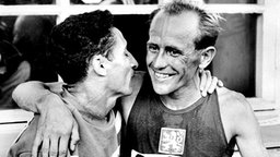 Die "tschechische Lokomotive" Emil Zatopek (r) gewinnt in Helsinki den 5.000-Meter-Lauf in 14:06,6 min und wird kurz nach dem Zieleinlauf vom zweitplatzierten Franzosen Alain O'Kacha Mimoun beglückwünscht. © picture-alliance / dpa 