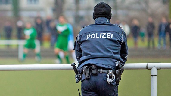 Ein Polizist steht an der Balustrade eines Amateurfußball-Platzes © IMAGO / Sebastian Wells 