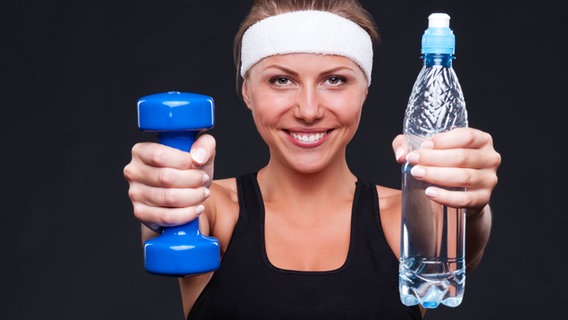 Eine Frau in Sportkleidung hält ein Gewicht und eine Wasserflasche. © Colourbox Foto: -