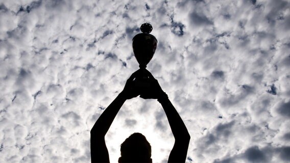 Eine Person hält einen Pokal gen Himmel. © .marqs / Photocase Foto: .marqs