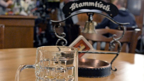 Ein Bierglas und ein Stammtischaschenbecher mit Glocke stehen auf einem Tisch in einer Kneipe. © picture alliance / dpa Foto: Winfried Rothermel