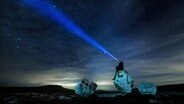Eine Person sitzt auf einem Felsen unter einem Sternenhimmel. Auf dem Kopf trägt sie eine Vorrichtung, aus der ein Lichtkegel hervorschießt. © picture alliance / empics | Danny Lawson Foto: Danny Lawson