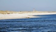 Ein langgestreckter Strand mit Dünen und einem Leutturm im Hintergrund © Kurverwaltung List Foto: Annika Orchowski
