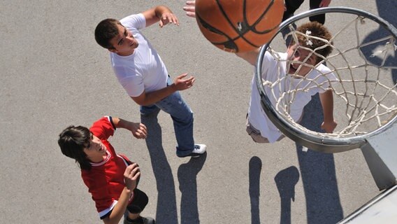 Drei Jugendliche spielen Basketball und blicken zum Korb hinauf. © Colourbox 