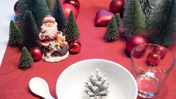 Ein Weihnachtsmann, Tannen und rote Weihnachtskugeln schmücken den Tisch für Kinder. © NDR Foto: Anja Deuble