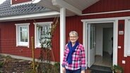 Ingrid Schilling steht vor dem Eingang eines roten Holzhauses. © NDR Foto: Frank Hajasch