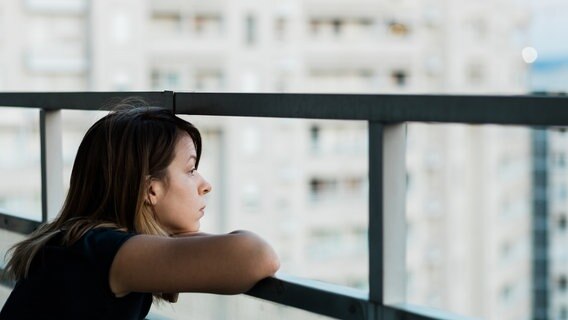 Eine junge Frau schaut traurig vom Balkon nach draußen. © Photocase Foto:  Marjan Apostolovic