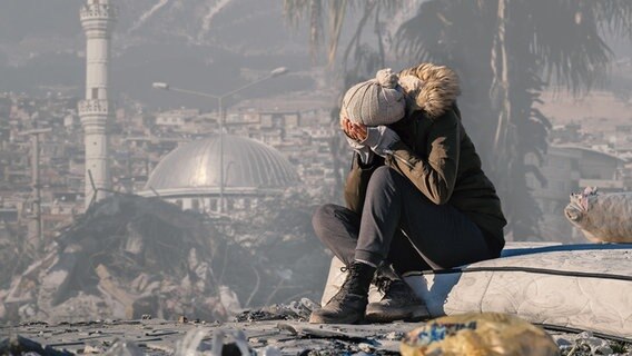 eine Frau sitzt auf einem Trümmerhaufen nach dem Erdbeben in der Türkei, Bildmontage © picture alliance / AA | Arif Hudaverdi Yaman, BR / Johannes Moths; Montage: BR Foto: Hudaverdi Yaman, BR / Johannes Moths; Montage: BR