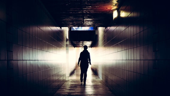 Gegenlichtaufnahme eines Menschen der einen spärlich beleuchteten Tunnel entlanggeht. © Photocase Foto:  tosini