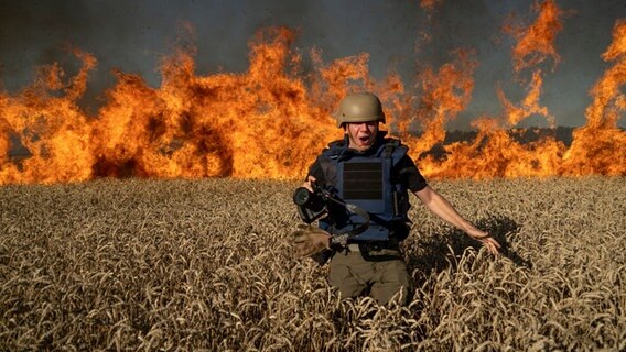 Der Fotojournalist Evgeniy Maloletka läuft vor dem Feuer in einem nach russischem Beschuss brennenden Weizenfeld während seines Einsatzes weg, einige Kilometer von der ukrainisch-russischen Grenze entfernt in der Region Charkiw. © AP/dpa Foto: Mstyslav Chernov