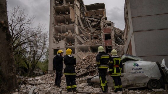Tschernihiw: Feuerwehrleute stehen vor einem Gebäude, das durch russische Angriffe teilweise zerstört wurde. © DPA Foto: Francisco Seco/AP/dpa