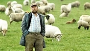 Schauspieler Bjarne Mädel auf einer Wiese mit Schafen. © Silberling Foto: Wiebke Schuster