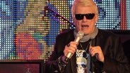 Heino singt bei der Uraufführung von Songs seiner neuen CD im NDR Landesfunkhaus Hamburg, hinter ihm zeigt eine Videoleinwand einen bunten Totenkopf mit Sonnenbrille. © NDR Foto: Daniel Sprenger