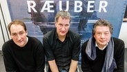 Reimer Bustorff (l-r), Musiker der Band Kettcar, Marcus Wiebusch, Musiker der Band Kettcar, und Daniel Karasek, Generalintendant des Schauspiels Kiel, posieren am 11.01.2016 in Kiel (Schleswig-Holstein) vor dem Plakat zur Inszenierung "Die Räuber". © dpa-Bildfunk Foto: Markus Scholz