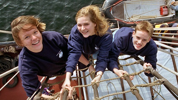 Ausbilderin Nicole Malter (Mitte) zeigt zwei Schülern am 30. Oktober 1999 auf dem Segelschiff "Thor Heyerdal" in Wilhelmshaven, wie man in die Wanten steigt. © Ulrich Perrey/picture alliance Foto: Ulrich Perrey