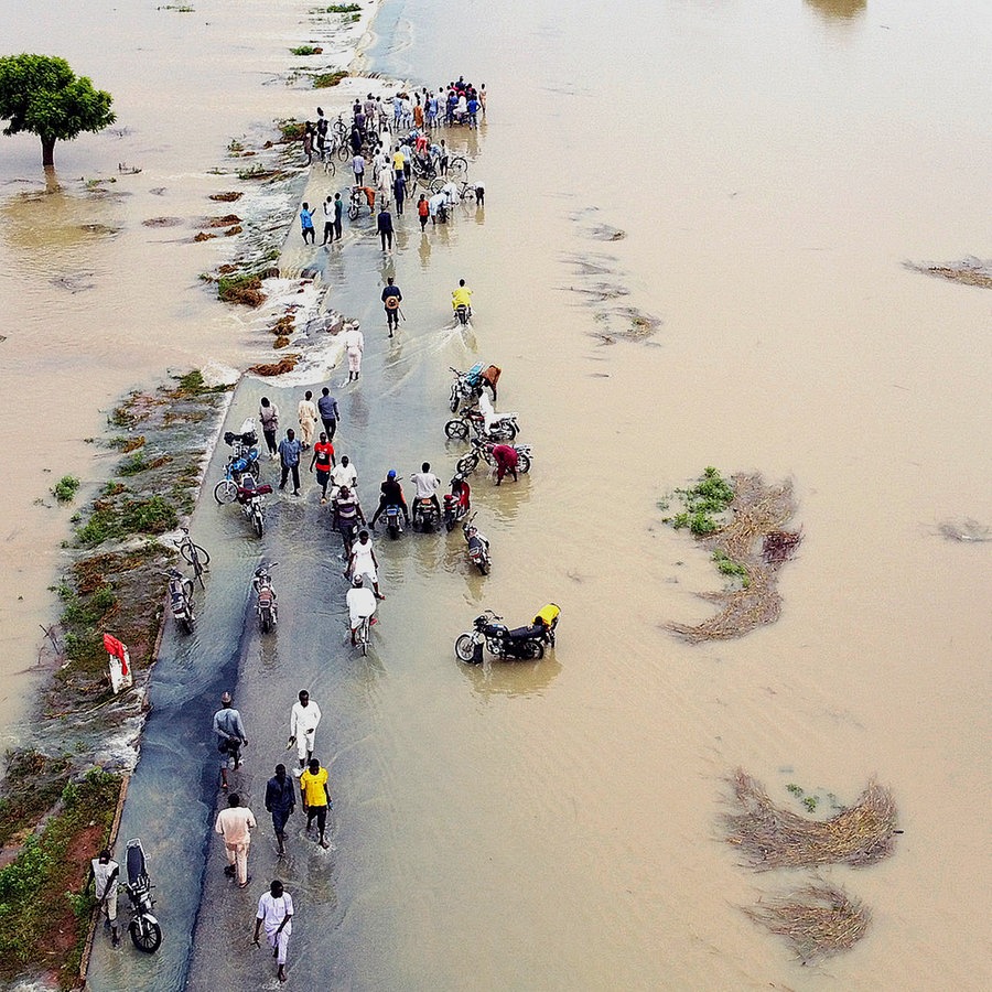 Menschen in Nigeria gehen nach heftigen Regenfällen über eine teils überschwemmte Straße. © dpa 